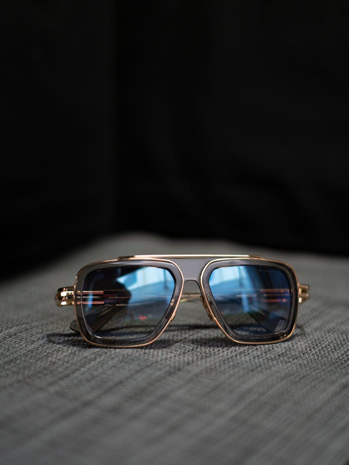 digital Elegant aviator sunglasses with blue lenses and gold frame on a textured grey surface.